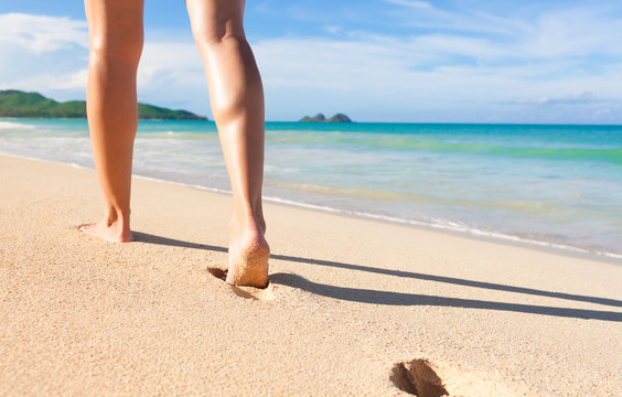 Beach travel - woman walking on sand beach leaving footprints in the sand.  Location Hawaii, Oahu.
