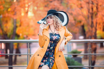 Obraz premium Beautiful stylish woman in a yellow coat and hat with long walks through fields autumn city,business women,lady in the city,creative computer colors,fashionable toning