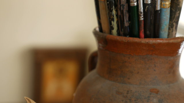 Artist paintbrushes. Set of different artist paint brushes in old crock with pumpkin close-up. Art studio concept. Selective focus footage with shallow DOF. 4K UHD video footage.
