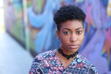 Pretty short hair girl with gray jacket posing against a fancy colorful wall
