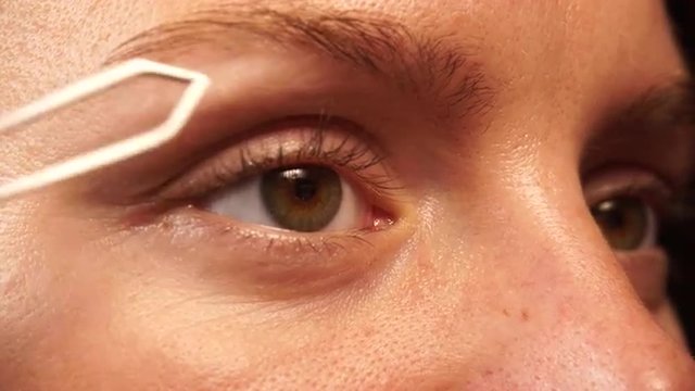 Woman tweezing eyebrows depilating with tweezers 4K