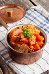 stew of beef with vegetables in a copper pot closeup