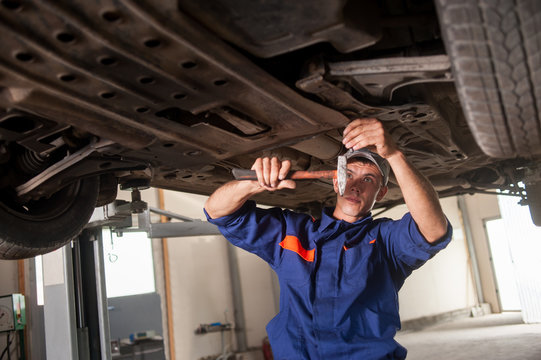 Portrait of car mechanic working with tools under car in automob