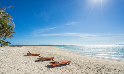 Fototapeta na wymiar Tropical vacation. Turquoise sea, 3 deckchairs, white sand and palms , sun - very beautiful beach.