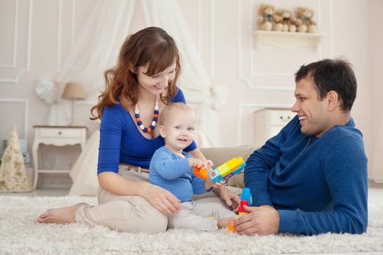 Young parents and cute son play building kit sitting on a carpet in children room