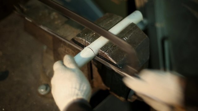 Man sawing with a manual hacksaw the pipe, gripped in a vise installed on the workbench
