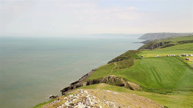 Calm sea and hazy summer coastal landscape of Ceredigion, Wales near Cardigan, looking north. A section of the Wales Coast path is visible along the cliff tops.