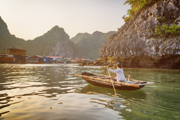 Fototapeta na wymiar Woman in boat returns to fishing village in the Ha Long Bay