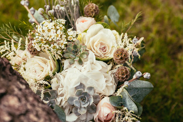 wedding bouquet with roses and succulents on green grass and woo