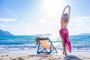 Woman in sarong stretching on the tropical beach - obrazy, fototapety, plakaty