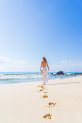 Beautiful woman walking on the beach with her footprints back