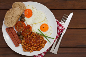 fried eggs with bread, sausages and beans on white plate