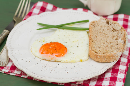 fried egg heart with green onion on white plate on green background