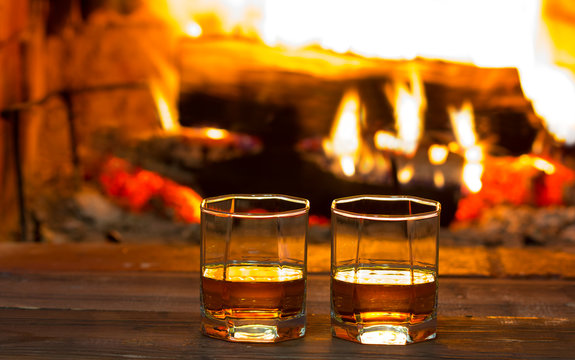 Two glasses of alcoholic drink in front of warm fireplace. Magical relaxed cozy atmosphere near  fire.
