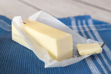 Gordijnen Stick of unwrapped butter on blue cloth © littleny