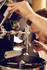 Man operating a modern coffee roasting machine and smelling the 