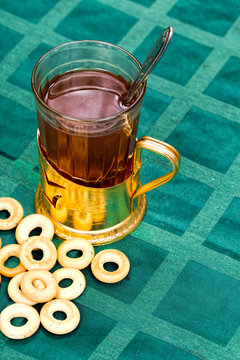 Glass Cup Of Tea In An Aluminum Cup Holder With Fragrant Green Bagels On Tablecloth