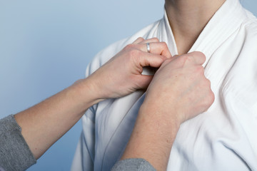 Hands of a parent who helps a child with a uniform for martial arts