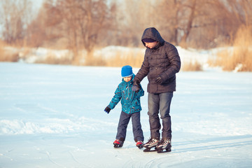 father and little son learning to skate in winter snow.