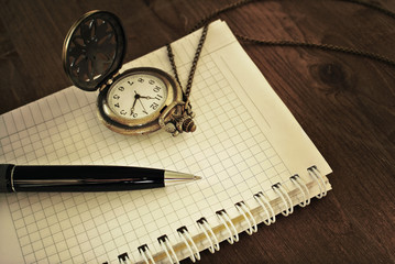 Notebook with blank pages, black pen and vintage pocket watch on dark background