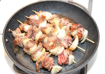 four shashlik skewers roasting in a frying pan