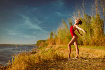 The young ballerina in a red bathing suit dances on the tips of