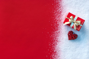 Holiday gift and red heart in the snow with red paper background. Copy space for your text. St. Valentines Day concept or Christmas concept