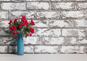 Red flowers in vase on the table on black and white brick wall background