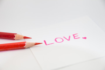 wording  "Love" in pink color with little heart on the small paper with red color pencils 
