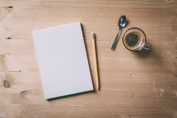 A recycled paper notebook checked with a black pencil with the eraser at the top and a cup of...