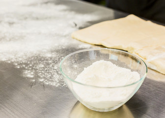 flour in a glass and a sheet of dough on a metal table in the kitchen