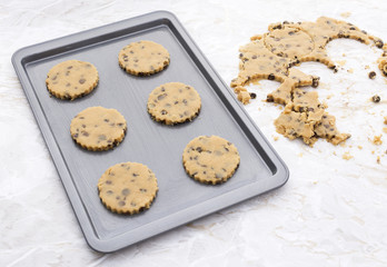 Six chocolate chip cookies on a baking tray