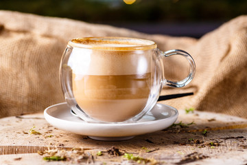 Glass thermo mug of cappuccino stands on the end of a tree.
