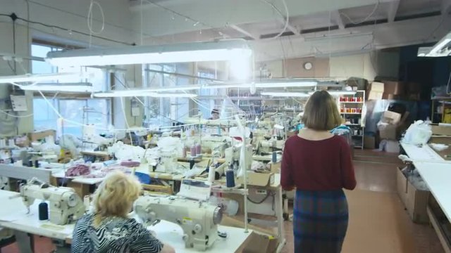 Young brunette woman with a tablet is shot from the back while walking through a clothing factory. Shot on RED Cinema Camera.