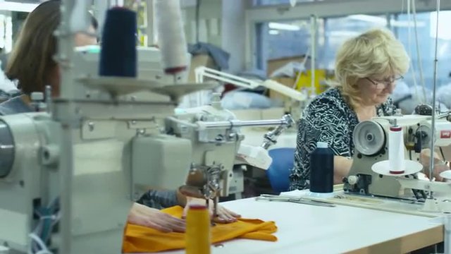 Motion shot of a senior and young garment workers sewing next to each other. Shot on RED Cinema Camera.