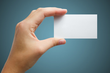 Obraz premium Hand holding white blank business visit card, gift, ticket, pass, present isolated on blue background. Copy space for text. Corporate identity package Template ID