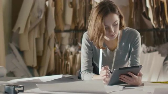 Clothing designer is using tablet while leaning on a studio table. Shot on RED Cinema Camera.