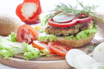 Homemade hamburger, vegetables and herbs.
Homemade hamburger, sliced tomatoes, onion, pepper, lettuce and dill on wooden board.