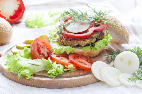 Homemade hamburger, vegetables and herbs.
Homemade hamburger, sliced tomatoes, onion, pepper, lettuce and dill on wooden board.
