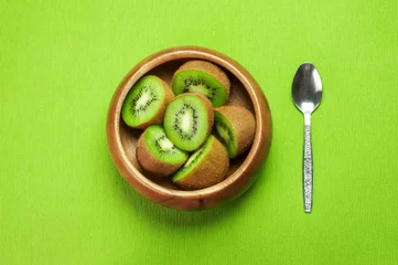 Zelfklevend Fotobehang Juicy ripe kiwi fruit in wooden bowl on green napkin with spoon © algae5