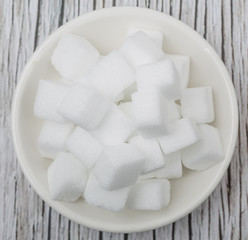 White sugar cube in white bowl over wooden background