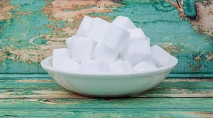 White sugar cube in white bowl over wooden background