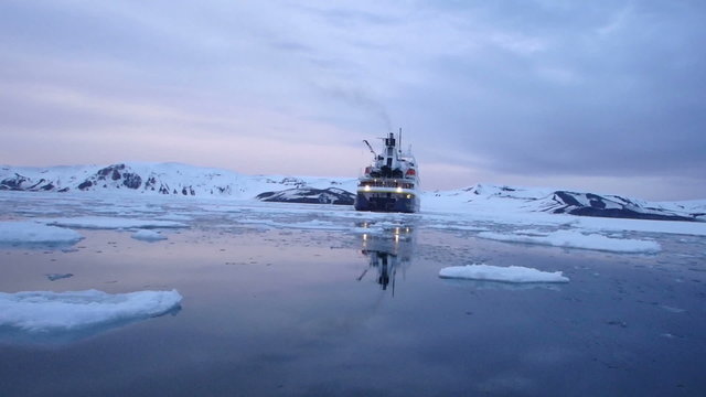 Cruise ship reflecting calm waters of Deception Bay, Antarctica at sunset.
