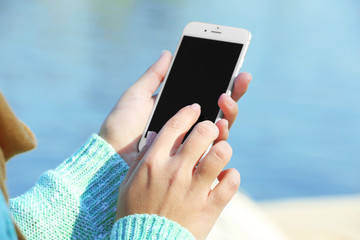 Female hands holding a mobile phone outdoors, on blurred background