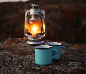 Decorative lamp and two blue mugs on rock in mountains