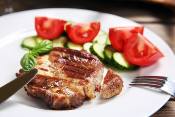 Roasted beef fillet and fresh vegetables on plate, on wooden background