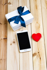 White Smart Phone With Blank Screen, White Gift Box With Blue Ribbon And Little Red Heart On Wooden Boards. Love Concept. 