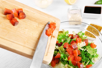 Female hands adding pieces of salmon into bowl with salad, close-up