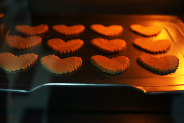 Uncooked heart shaped biscuits on a baking tray in an oven
