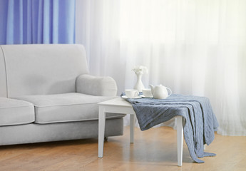 Sofa and little table with home decor in the room in front of the window with curtains